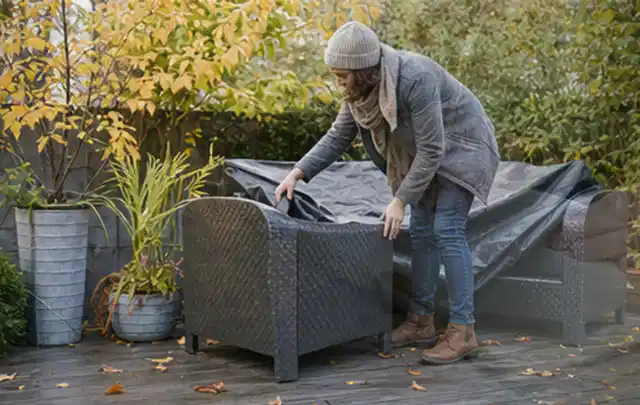 Person deckt Gartenmöbel vor der kalten Jahreszeit sorgfältig ab; Thema Gartenlounges, Schwerpunkt Checkliste; Praxisalltag.