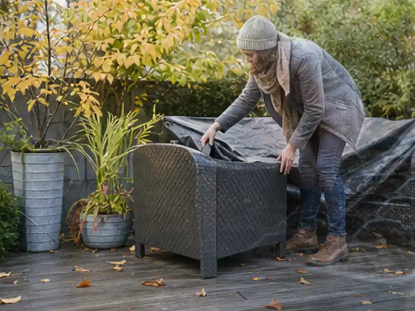 Person deckt Gartenmöbel vor der kalten Jahreszeit sorgfältig ab; Thema Gartenlounges, Schwerpunkt Dimensionierung; Titelbild.