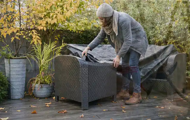 Person deckt Gartenmöbel vor der kalten Jahreszeit sorgfältig ab; Thema Gartenlounges, Schwerpunkt Ersatzteile; Kontrolle.