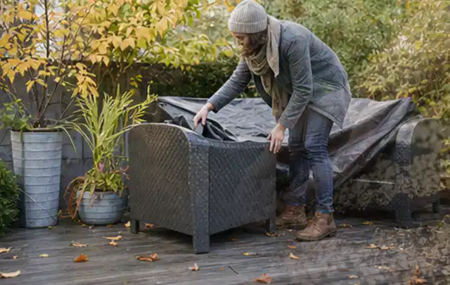 Person deckt Gartenmöbel vor der kalten Jahreszeit sorgfältig ab; Thema Gartenlounges, Schwerpunkt Gärten mit kleiner Fläche; Praxisalltag.