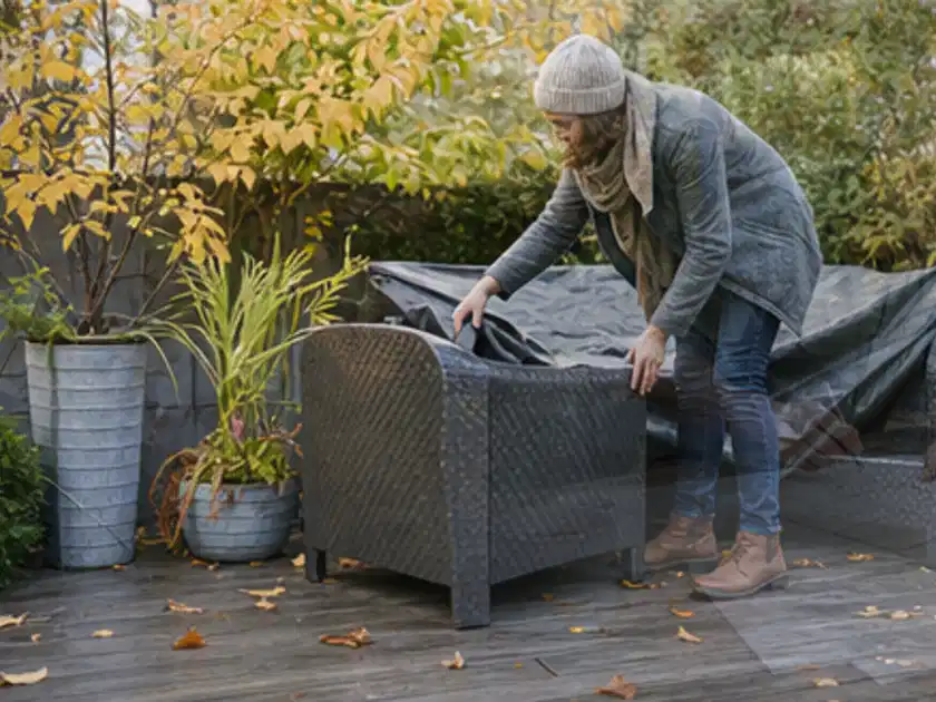 Person deckt Gartenmöbel vor der kalten Jahreszeit sorgfältig ab; Thema Gartenlounges, Schwerpunkt Nachhaltigkeit; Titelbild.