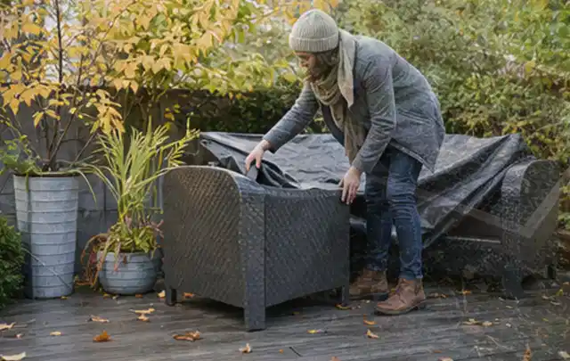 Person deckt Gartenmöbel vor der kalten Jahreszeit sorgfältig ab; Thema Gartenlounges, Schwerpunkt Reinigung; Ausgangslage.