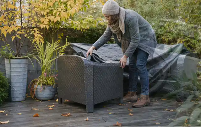 Person deckt Gartenmöbel vor der kalten Jahreszeit sorgfältig ab; Thema Gartenlounges, Schwerpunkt Wartung; Kontrolle.
