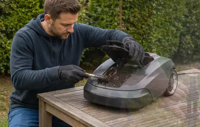Person wartet einen geöffneten Mähroboter auf einem stabilen Gartentisch; Thema Gartenpumpen, Schwerpunkt Wartung; Kontrolle.