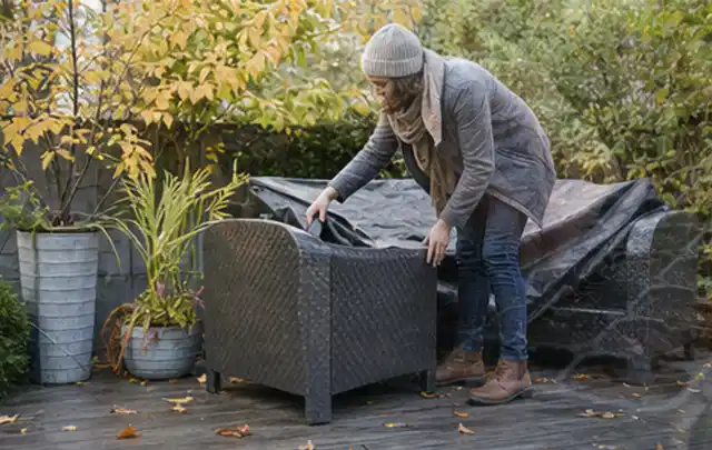 Person deckt Gartenmöbel vor der kalten Jahreszeit sorgfältig ab; Thema Gartenstühle, Schwerpunkt Anwendung; Umsetzung.