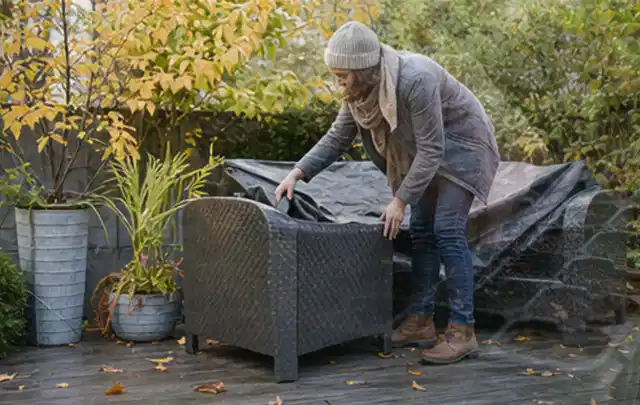 Person deckt Gartenmöbel vor der kalten Jahreszeit sorgfältig ab; Thema Gartenstühle, Schwerpunkt Gärten mit großer Fläche; Kontrolle.