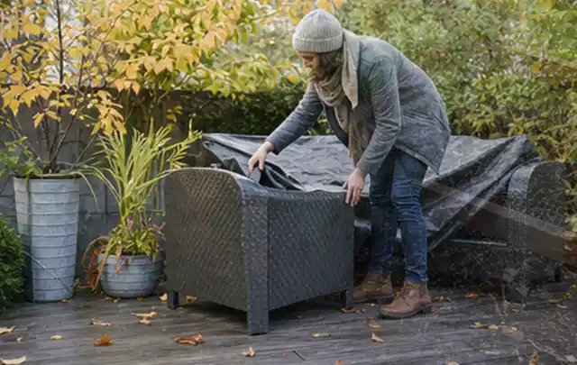 Person deckt Gartenmöbel vor der kalten Jahreszeit sorgfältig ab; Thema Gartenstühle, Schwerpunkt Winterlager; Kontrolle.