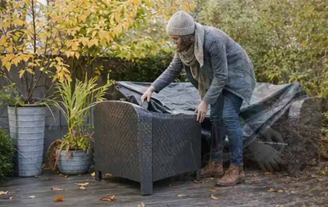 Person deckt Gartenmöbel vor der kalten Jahreszeit sorgfältig ab; Thema Gartentische, Schwerpunkt Bestenliste; Umsetzung.