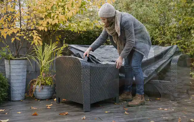 Person deckt Gartenmöbel vor der kalten Jahreszeit sorgfältig ab; Thema Gartentische, Schwerpunkt Checkliste; Umsetzung.
