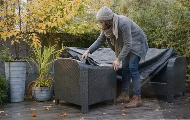 Person deckt Gartenmöbel vor der kalten Jahreszeit sorgfältig ab; Thema Gartentische, Schwerpunkt Kaufberatung; Umsetzung.