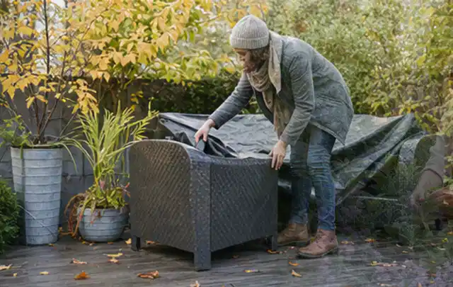 Person deckt Gartenmöbel vor der kalten Jahreszeit sorgfältig ab; Thema Gartentische, Schwerpunkt Reinigung; Praxisalltag.