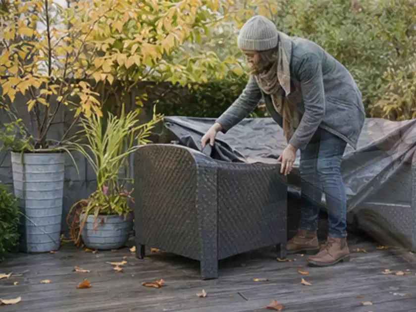 Person deckt Gartenmöbel vor der kalten Jahreszeit sorgfältig ab; Thema Gartentische, Schwerpunkt Reparatur; Titelbild.
