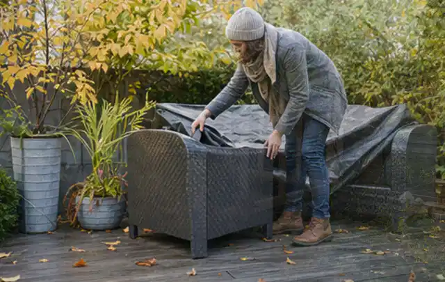 Person deckt Gartenmöbel vor der kalten Jahreszeit sorgfältig ab; Thema Gartentische, Schwerpunkt Vergleich; Kontrolle.