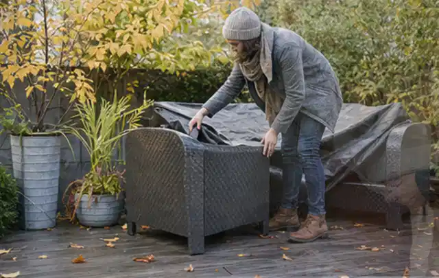 Person deckt Gartenmöbel vor der kalten Jahreszeit sorgfältig ab; Thema Gartentische, Schwerpunkt Winterlager; Kontrolle.