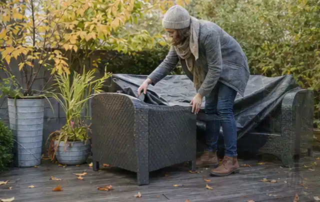 Person deckt Gartenmöbel vor der kalten Jahreszeit sorgfältig ab; Thema Gasgrills, Schwerpunkt Anwendung; Praxisalltag.
