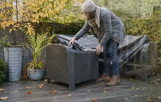 Person deckt Gartenmöbel vor der kalten Jahreszeit sorgfältig ab; Thema Gasgrills, Schwerpunkt Nachhaltigkeit; Praxisalltag.