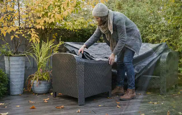 Person deckt Gartenmöbel vor der kalten Jahreszeit sorgfältig ab; Thema Gasgrills, Schwerpunkt Outdoor Freizeit; Umsetzung.