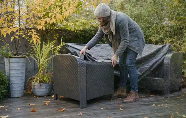 Person deckt Gartenmöbel vor der kalten Jahreszeit sorgfältig ab; Thema Gasgrills, Schwerpunkt Reparatur; Kontrolle.
