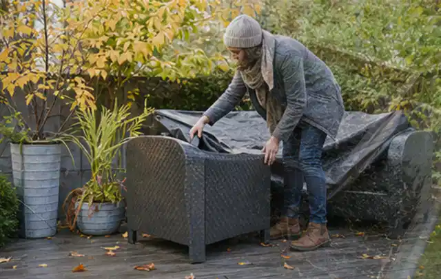 Person deckt Gartenmöbel vor der kalten Jahreszeit sorgfältig ab; Thema Gasgrills, Schwerpunkt Sicherheit; Kontrolle.