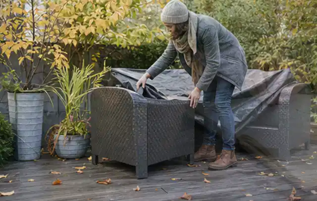 Person deckt Gartenmöbel vor der kalten Jahreszeit sorgfältig ab; Thema Gasgrills, Schwerpunkt Systemvergleich; Kontrolle.