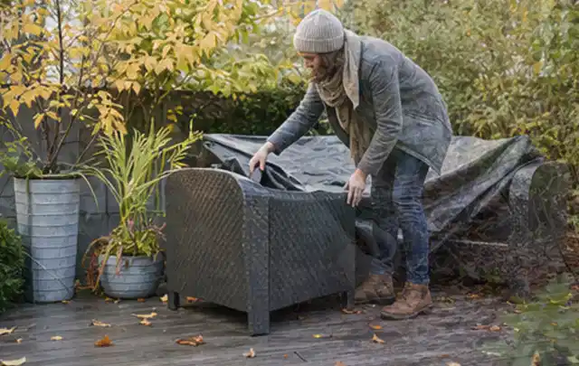 Person deckt Gartenmöbel vor der kalten Jahreszeit sorgfältig ab; Thema Gasgrills, Schwerpunkt Wartung; Ausgangslage.