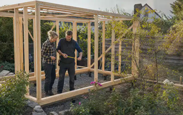 Person plant den Bau eines Gartenhauses auf einer vorbereiteten Fläche; Thema Geräteschuppen, Schwerpunkt Fehlerhilfe; Praxisalltag.