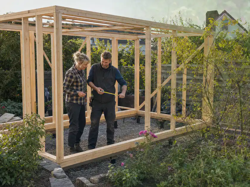 Person plant den Bau eines Gartenhauses auf einer vorbereiteten Fläche; Thema Geräteschuppen, Schwerpunkt Materialwahl; Titelbild.
