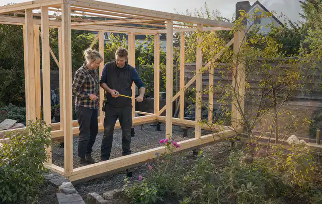Person plant den Bau eines Gartenhauses auf einer vorbereiteten Fläche; Thema Geräteschuppen, Schwerpunkt Pflege; Praxisalltag.