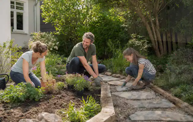Familie geht auf einem Weg durch einen abwechslungsreich gestalteten Garten; Thema Hanggarten, Schwerpunkt Naturgarten; Praxisalltag.