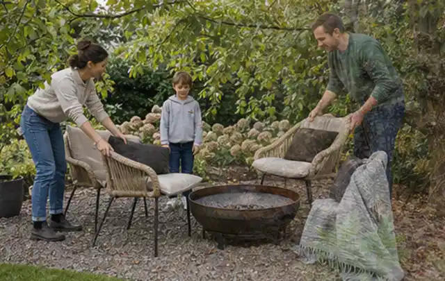 Familie stellt wetterfeste Sessel an einem geschützten Sitzplatz im Garten auf; Thema Hanggarten, Schwerpunkt Privatsphäre; Umsetzung.