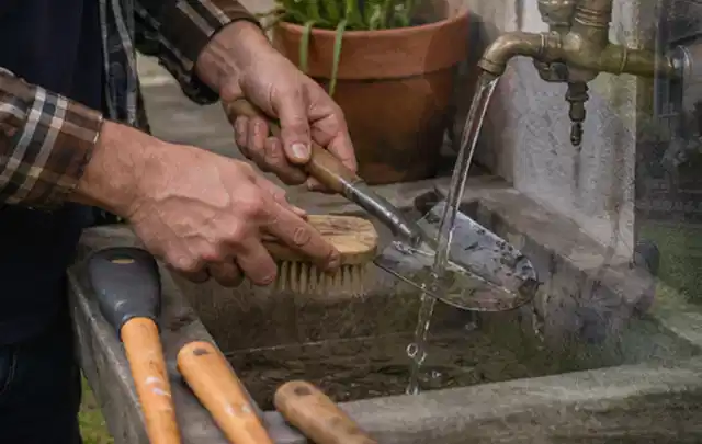 Hände reinigen gebrauchte Gartengeräte mit Bürste und Wasser am Außenbecken; Thema Heckenscheren, Schwerpunkt Gärten mit kleiner Fläche; Praxisalltag.
