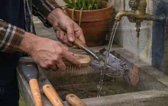 Hände reinigen gebrauchte Gartengeräte mit Bürste und Wasser am Außenbecken; Thema Heckenscheren, Schwerpunkt Gartengeräte; Ergebnis.