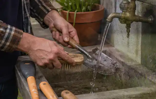 Hände reinigen gebrauchte Gartengeräte mit Bürste und Wasser am Außenbecken; Thema Heckenscheren, Schwerpunkt Kosten; Ergebnis.