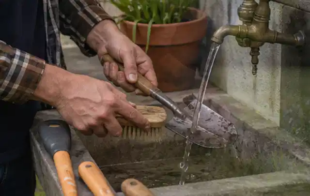 Hände reinigen gebrauchte Gartengeräte mit Bürste und Wasser am Außenbecken; Thema Heckenscheren, Schwerpunkt Leistung; Umsetzung.