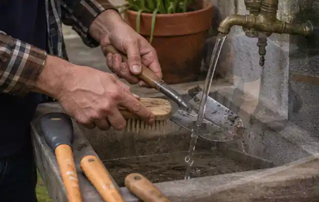 Hände reinigen gebrauchte Gartengeräte mit Bürste und Wasser am Außenbecken; Thema Heckenscheren, Schwerpunkt Nachhaltigkeit; Umsetzung.