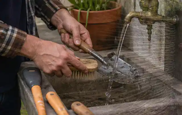 Hände reinigen gebrauchte Gartengeräte mit Bürste und Wasser am Außenbecken; Thema Heckenscheren, Schwerpunkt Winterlager; Ausgangslage.