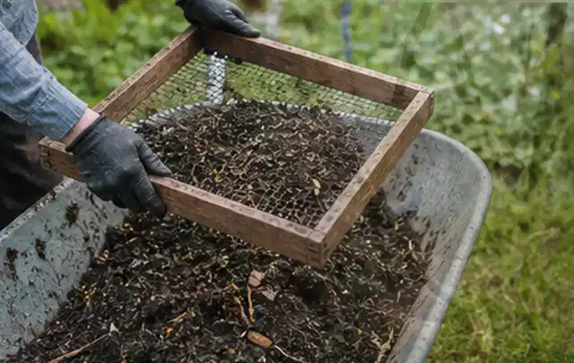 Behandschuhte Hände sieben reifen Kompost über einer Gartenschubkarre; Thema Hochbeet für den Balkon, Schwerpunkt Nachhaltigkeit; Ausgangslage.