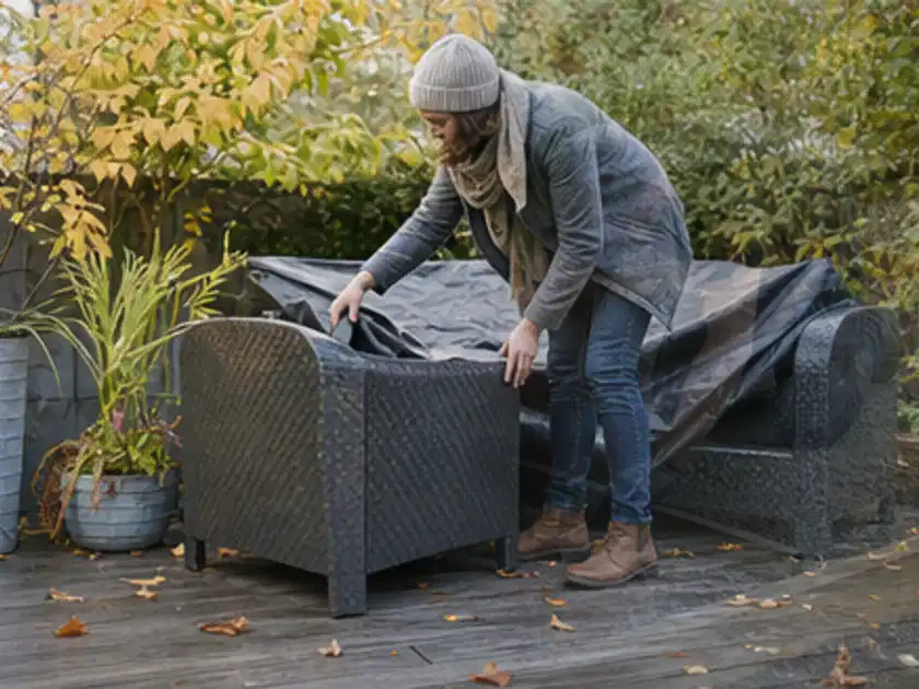 Person deckt Gartenmöbel vor der kalten Jahreszeit sorgfältig ab; Thema Hollywoodschaukeln, Schwerpunkt Winterlager; Titelbild.