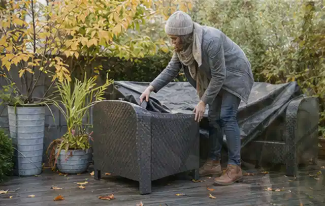 Person deckt Gartenmöbel vor der kalten Jahreszeit sorgfältig ab; Thema Holzkohlegrills, Schwerpunkt Nachhaltigkeit; Umsetzung.