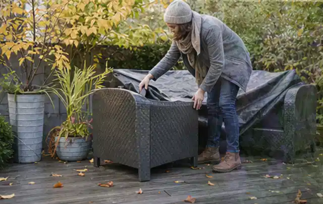 Person deckt Gartenmöbel vor der kalten Jahreszeit sorgfältig ab; Thema Holzkohlegrills, Schwerpunkt Reparatur; Kontrolle.