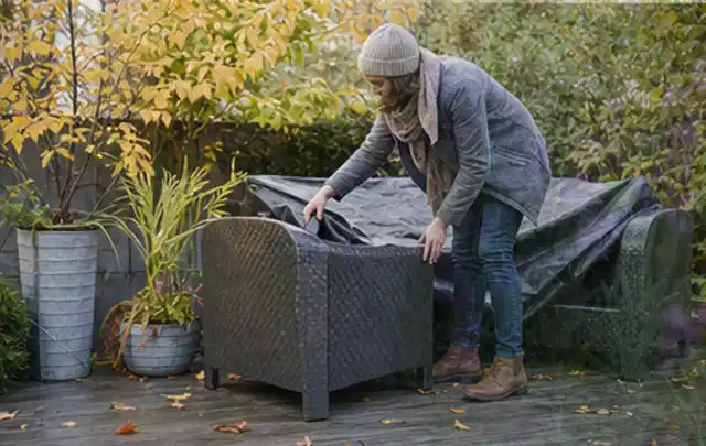 Person deckt Gartenmöbel vor der kalten Jahreszeit sorgfältig ab; Thema Holzkohlegrills, Schwerpunkt Vergleich; Kontrolle.