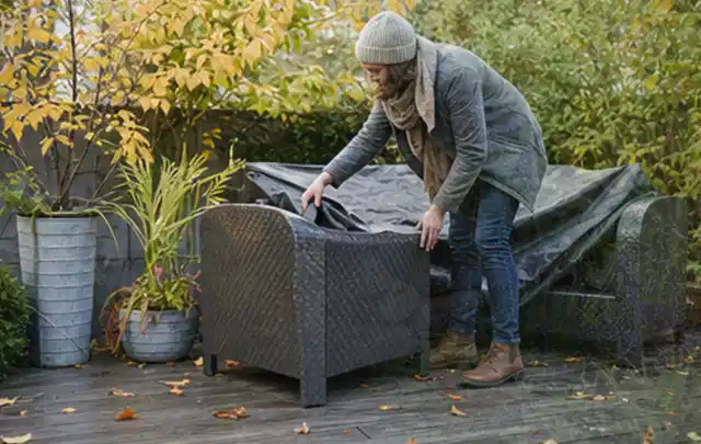 Person deckt Gartenmöbel vor der kalten Jahreszeit sorgfältig ab; Thema Holzkohlegrills, Schwerpunkt Winterlager; Ergebnis.