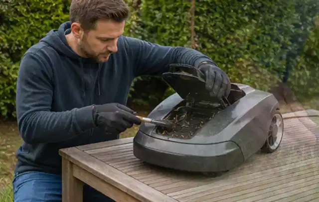 Person wartet einen geöffneten Mähroboter auf einem stabilen Gartentisch; Thema Holzspalter, Schwerpunkt Gartengeräte; Umsetzung.