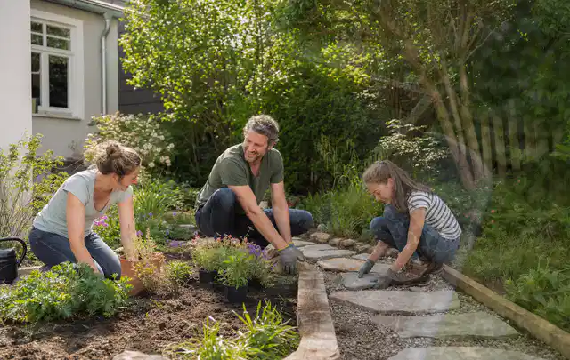 Familie geht auf einem Weg durch einen abwechslungsreich gestalteten Garten; Thema Holzzäune, Schwerpunkt DIY; Kontrolle.
