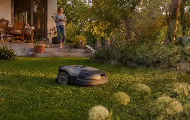 Mähroboter fährt am Abend über einen Rasen im Familiengarten; Thema Husqvarna Automower, Schwerpunkt Anwendung; Kontrolle.