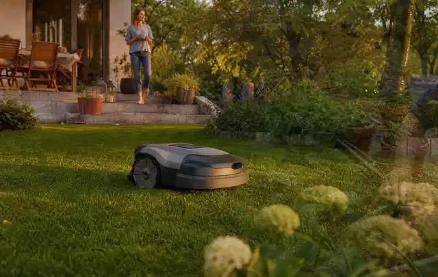 Mähroboter fährt am Abend über einen Rasen im Familiengarten; Thema Husqvarna Automower, Schwerpunkt Ersatzteile; Ergebnis.