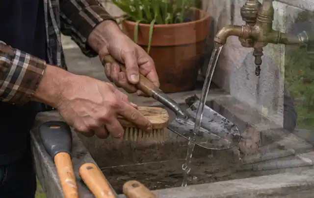 Hände reinigen gebrauchte Gartengeräte mit Bürste und Wasser am Außenbecken; Thema Husqvarna Automower, Schwerpunkt Gärten mit großer Fläche; Ergebnis.
