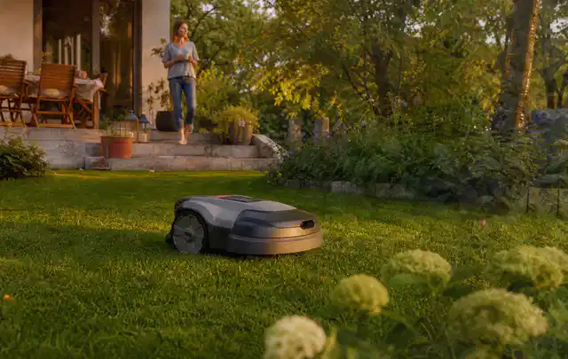 Mähroboter fährt am Abend über einen Rasen im Familiengarten; Thema Husqvarna Automower, Schwerpunkt Gärten mit kleiner Fläche; Umsetzung.