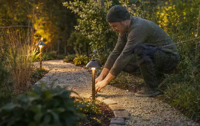Person richtet eine niedrige warm leuchtende Gartenlampe am Kiesweg aus; Thema Husqvarna Automower, Schwerpunkt Gärten mit kleiner Fläche; Ergebnis.