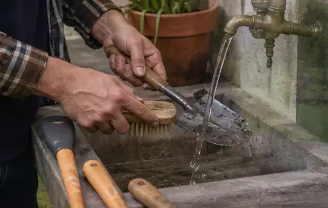 Hände reinigen gebrauchte Gartengeräte mit Bürste und Wasser am Außenbecken; Thema Husqvarna Automower, Schwerpunkt Reinigung; Ergebnis.